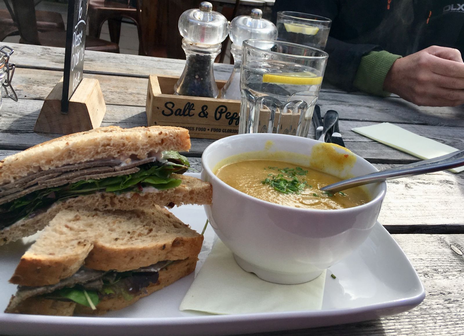Photograph of a bowl of lentil soup with a brown bread sandwich.